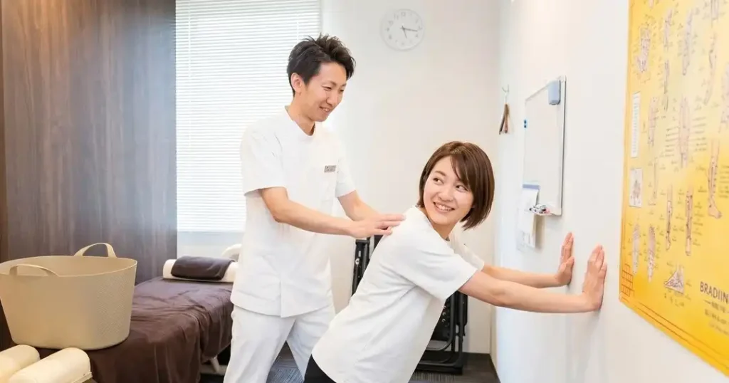 肩こりの根本改善に向け、院内で患者様に壁を使った簡単な腕立て伏せ（宿題）のフォームを丁寧に指導する札幌クラーク治療院の院長