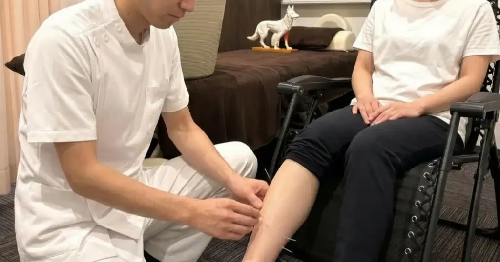 患者さんを椅子に座らせたまま、患部に触れずに足のツボ（GB35付近）へ遠隔鍼治療を行っている様子
